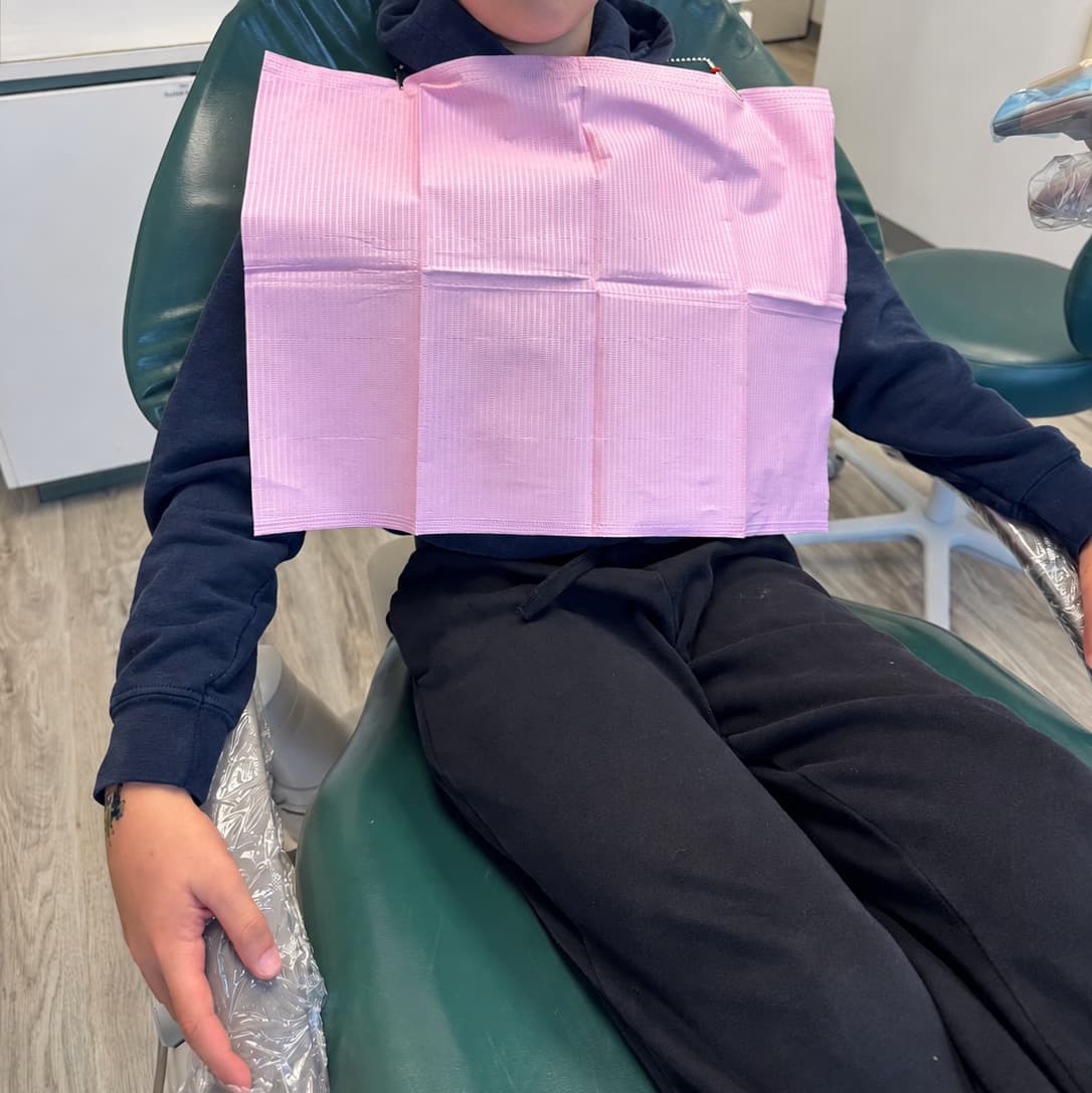 Enfant assis dans le fauteuil dentaire avec un bavoir rose